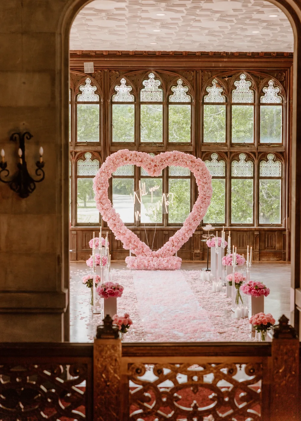 A blush rose heart seen through a carved stone arch, a pink petal aisle leading towards it