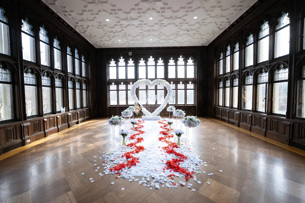 A white floral heart at the far end of a wood-panelled hall, a red and white petal aisle running to it between tall leaded windows