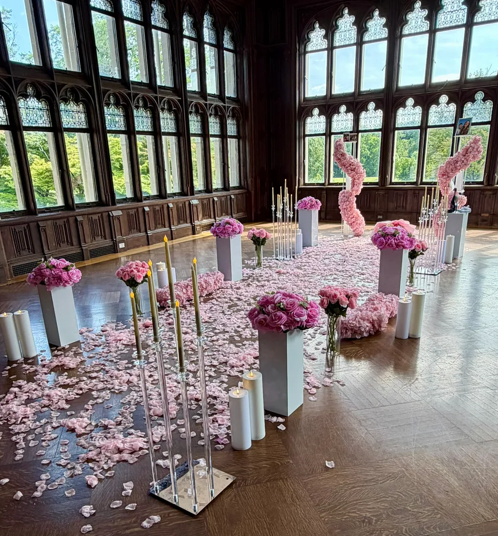 The same panelled hall dressed in blush, pink roses on tall stands above a carpet of pink petals