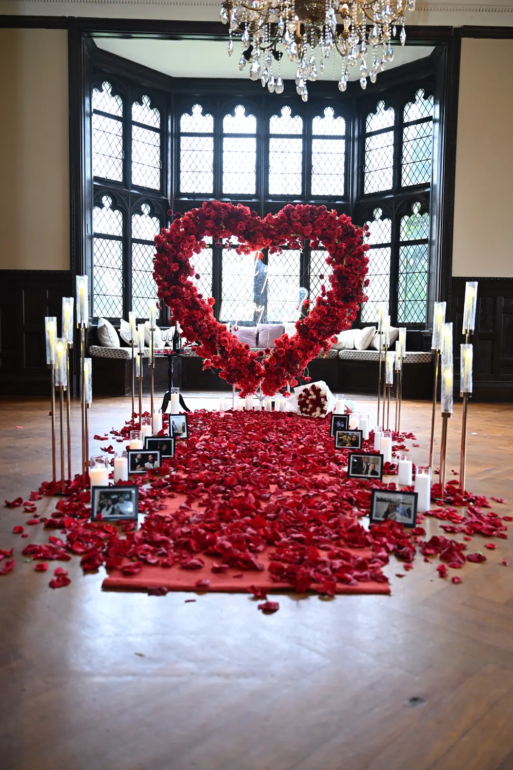 A red rose heart before tall gothic windows, with a petal aisle, candle stands and framed photographs