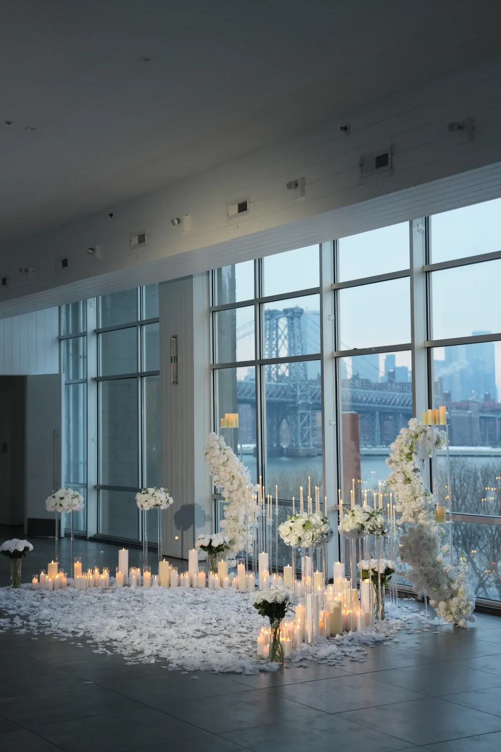 White florals and candles across the floor of an empty glass-walled venue
