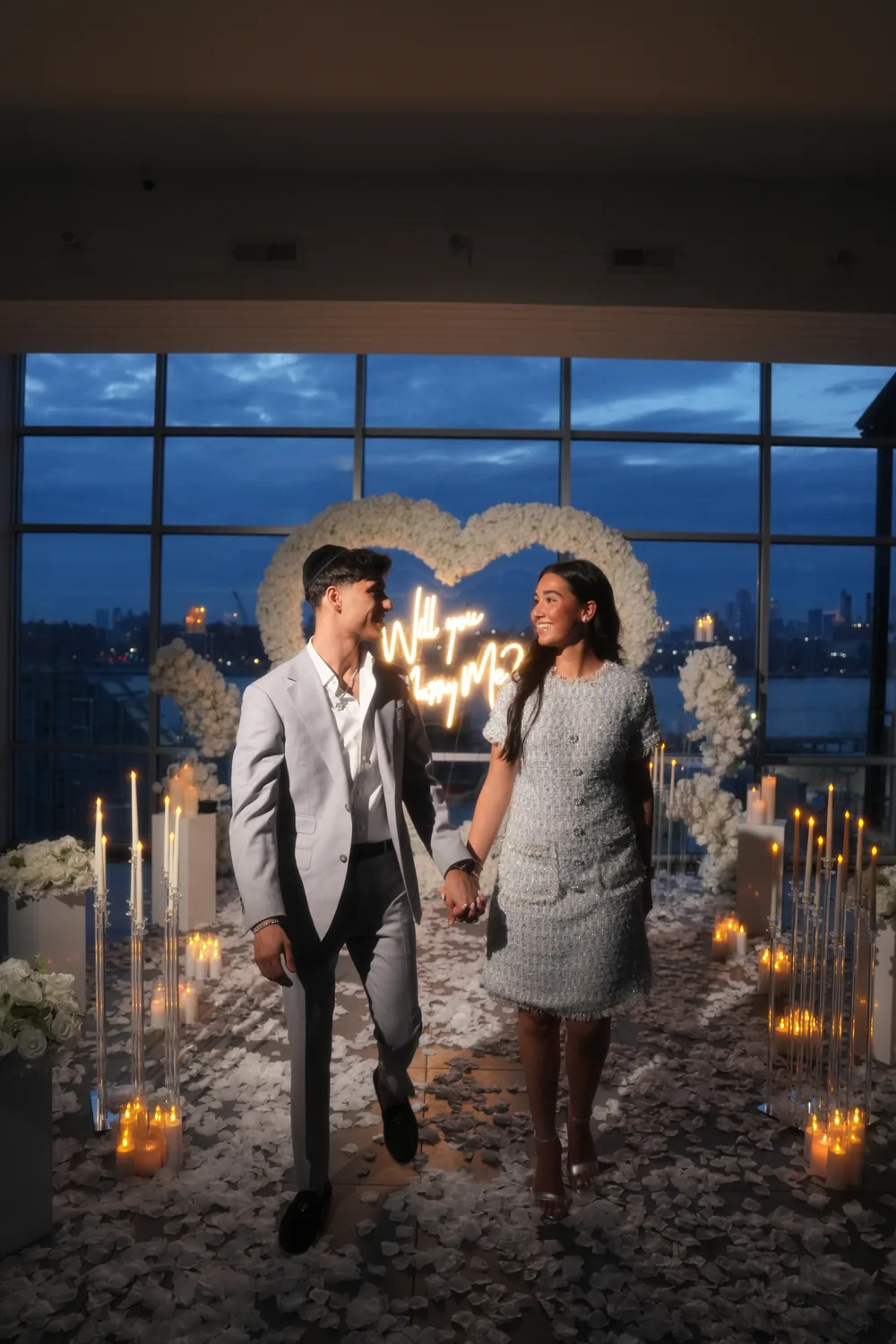 A couple walking through candles towards a white floral heart at night