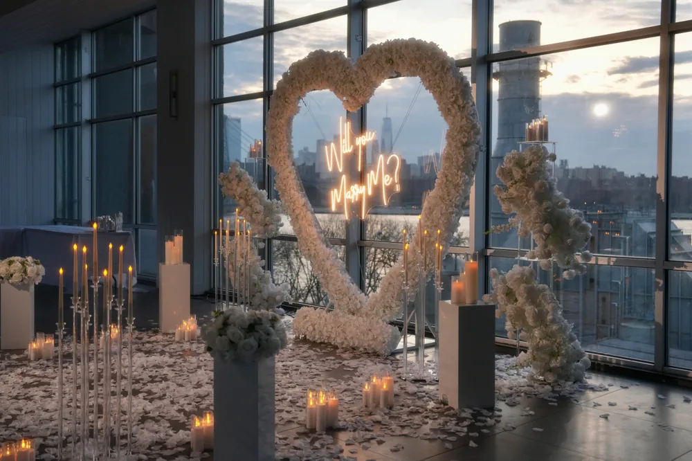 A white floral heart with a neon script sign in a glass-walled venue at sunset