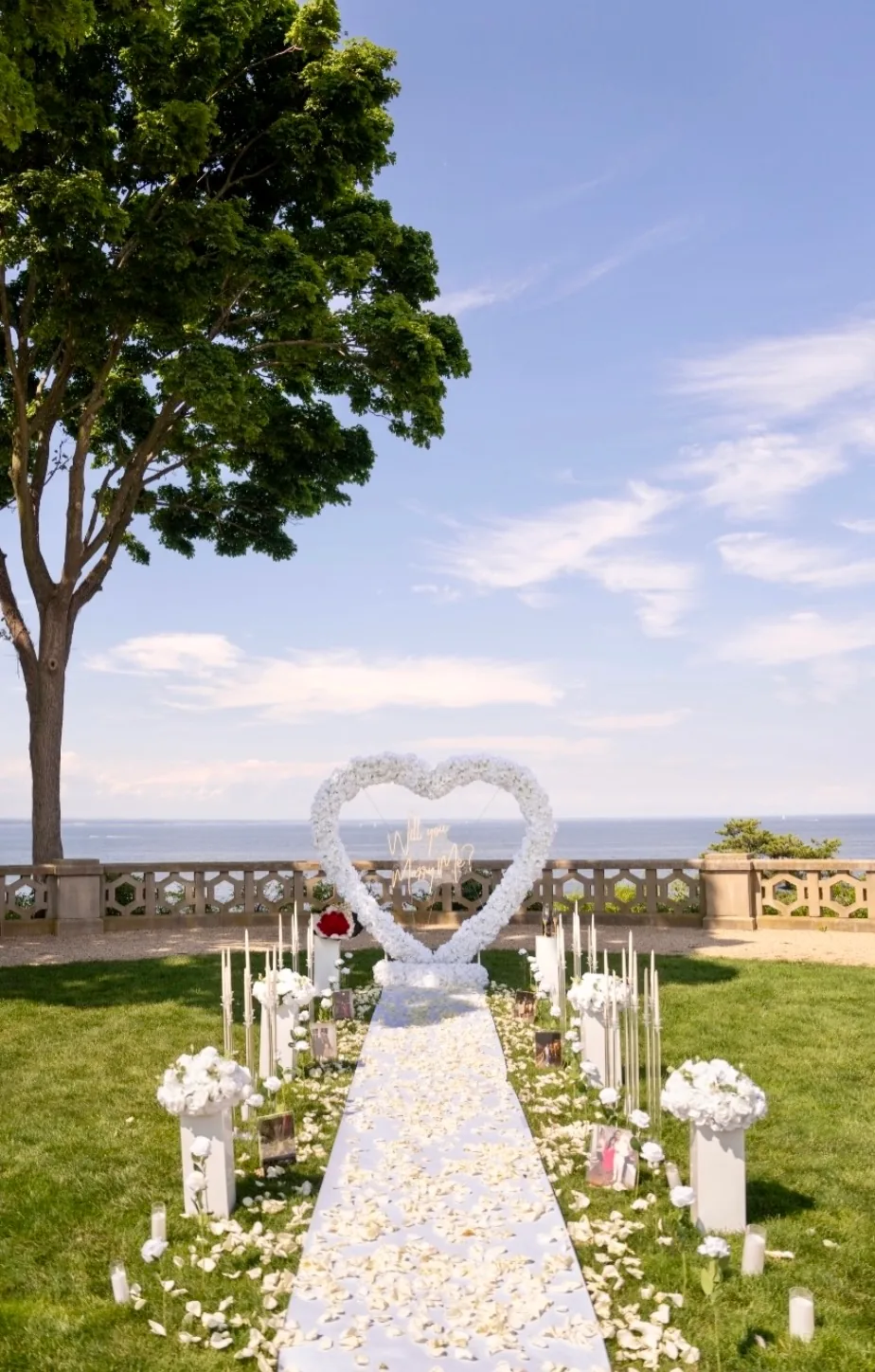 A white floral heart on a lawn under tall trees by the water