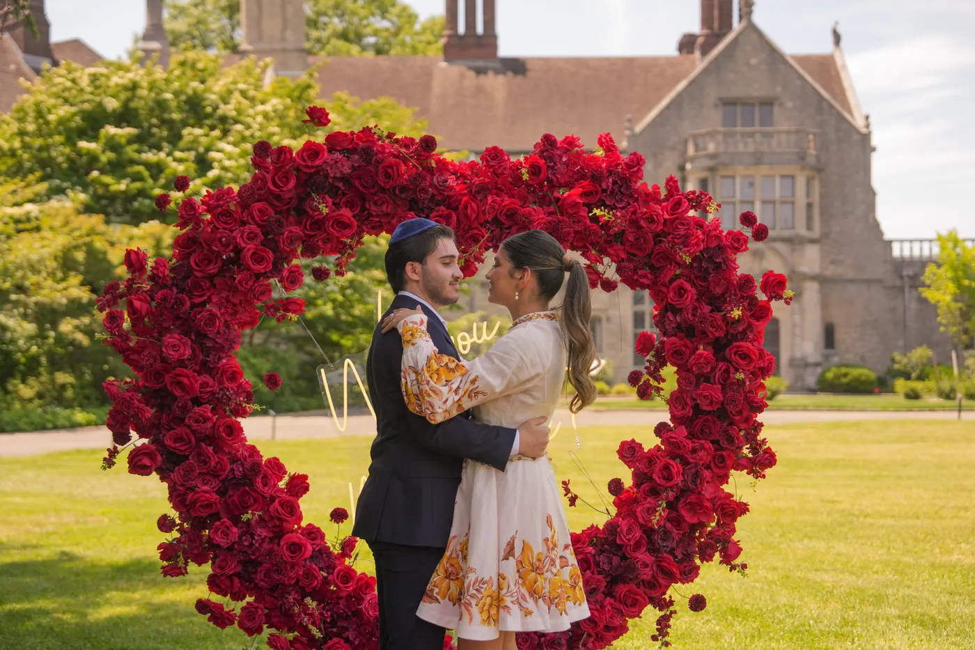 A couple embracing inside a red rose heart on the lawn of a stone estate