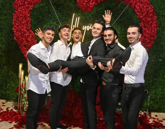 Friends cheering around the newly engaged couple in front of a red rose heart