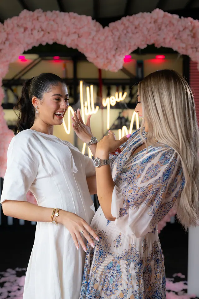 Two women laughing together as she holds up her ring hand