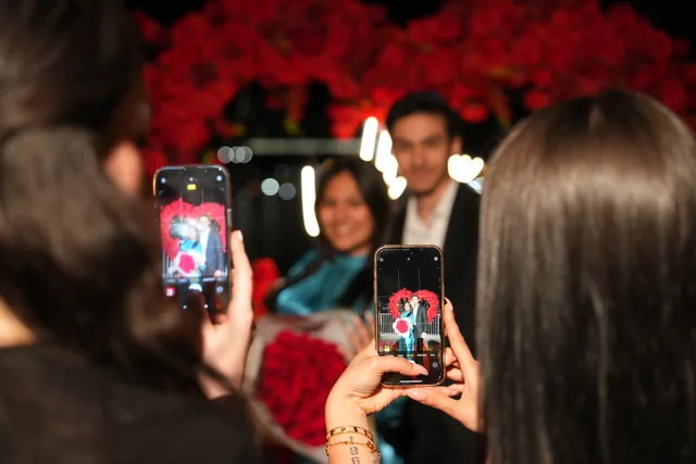 Guests holding up their phones to film the couple through a canopy of red roses