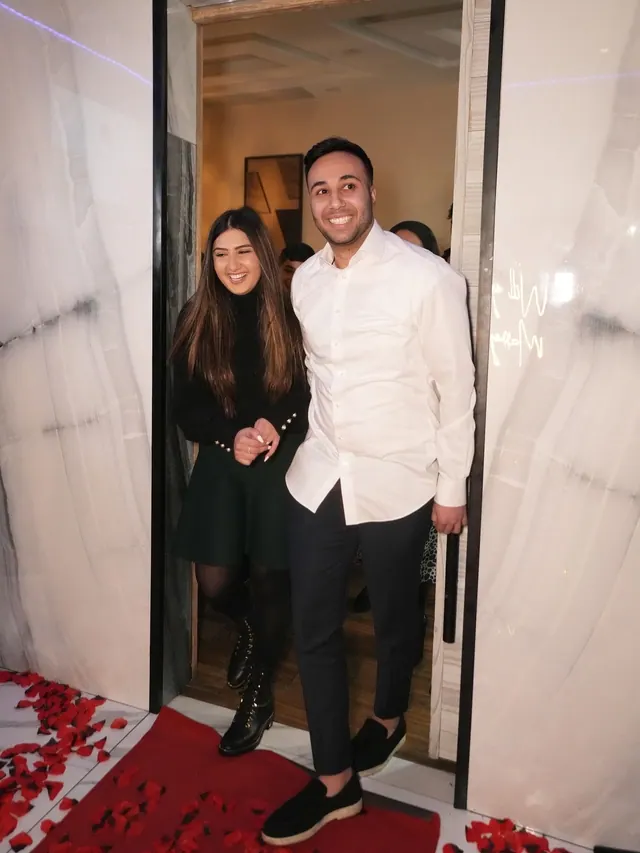 A couple walking in through a doorway, smiling, onto red rose petals
