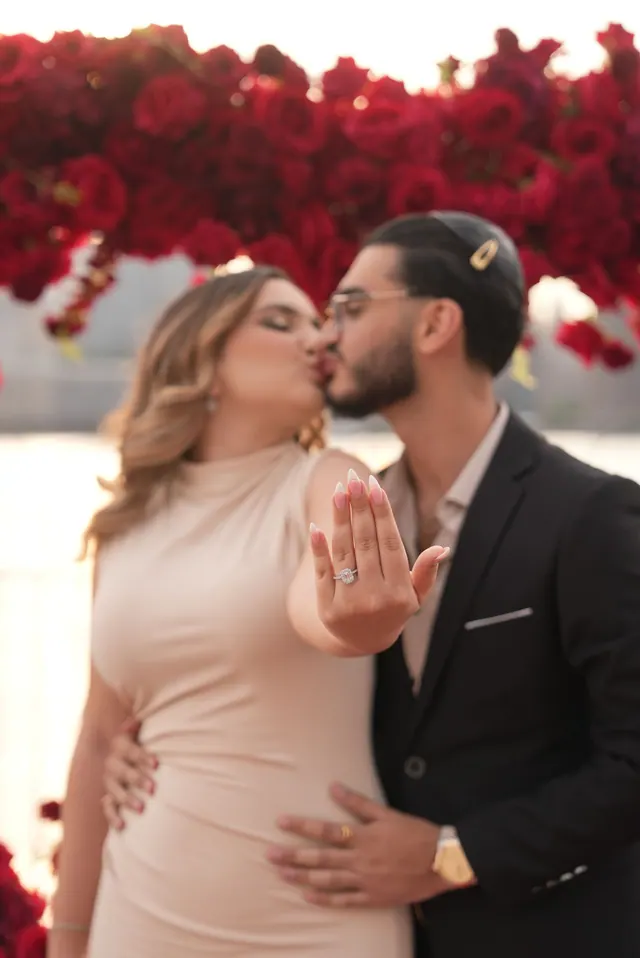 She kisses his cheek and shows her ring