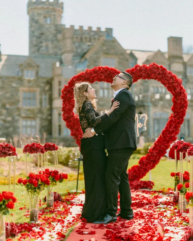 A couple hugging inside a red rose heart on the lawn of a stone estate