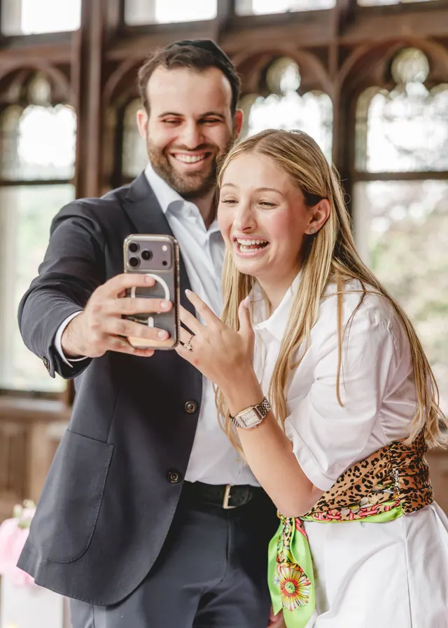 He takes a selfie as she laughs and shows her ring