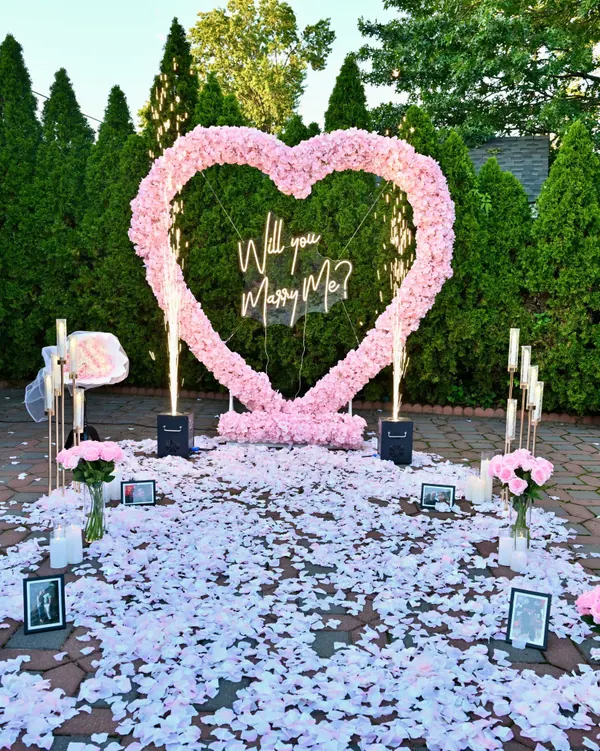 A pink rose heart with a Will You Marry Me sign in a garden courtyard edged with evergreens