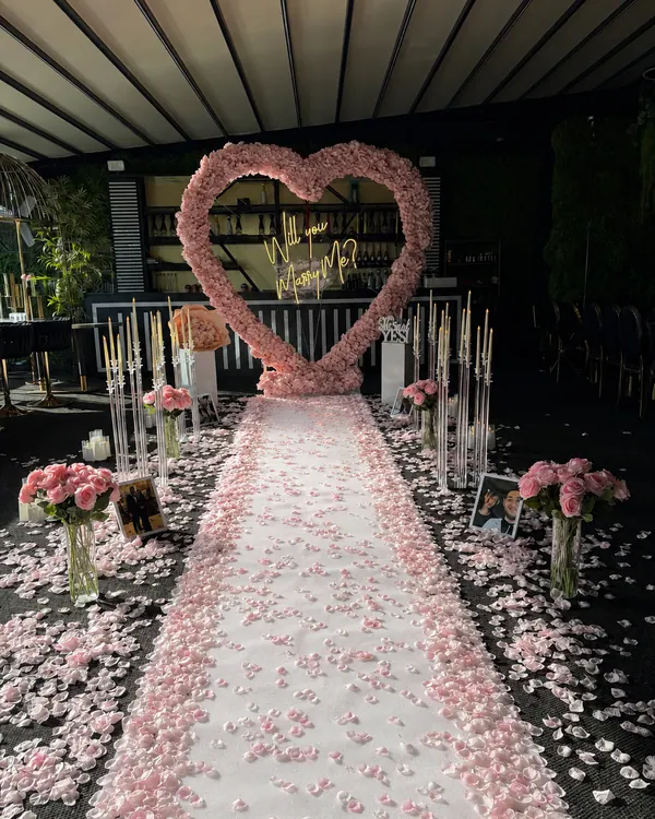 A pink rose heart at the end of a long pink petal aisle lined with candles in a dark room