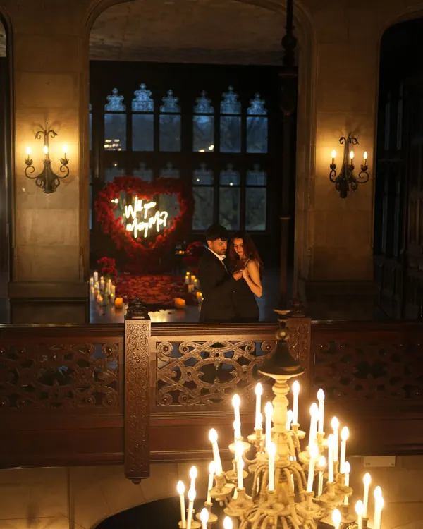 A red rose heart with a neon sign in a dark wood-panelled room lit by a candle chandelier