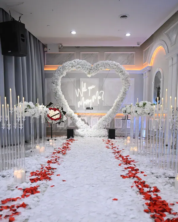 A white rose heart at the end of a petal aisle lined with glass stands in a white modern hall