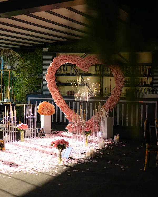 A pink rose heart with white petals and candles on a covered, planted terrace